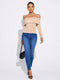 A woman modeling an off-the-shoulder beige long-sleeve top paired with blue skinny jeans, holding a black handbag against a plain white studio background.