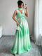A woman takes a mirror selfie wearing a sleeveless mint green to white ombré maxi dress with a halter neckline, a fitted waist, and a flowing skirt. She is holding a small white handbag in a room with gray tiled floors and white curtains.