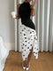 A woman models a sleeveless black and white polka dot wrap midi skirt with a high slit, paired with a black top and white pointed-toe heels, standing in front of white curtains.