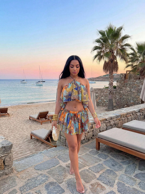 A woman wearing a colorful, patterned two-piece swimwear set with a halter top and matching mini skirt, walking on a stone path at a beach resort during sunset.