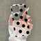 Clear phone case with black polka dots held by a hand against a neutral background