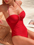 Woman wearing a red swimsuit with white straps on a sunlit beach.