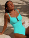 Woman in a turquoise swimsuit sitting on a sandy beach.