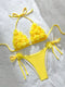 A bright yellow two-piece bikini set laid flat on a white fabric background. The triangle bikini top has textured, ruffled flower-like detailing on each cup and thin side ties.