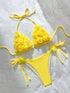 A bright yellow two-piece bikini set laid flat on a white fabric background. The triangle bikini top has textured, ruffled flower-like detailing on each cup and thin side ties.