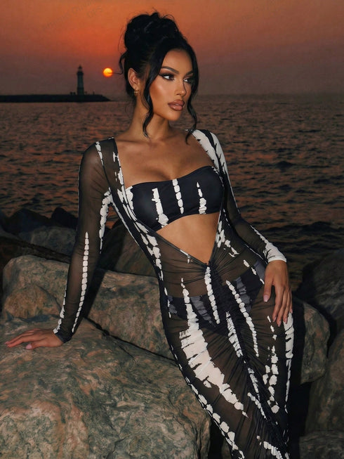 Woman in a black and white dress sitting on rocks by the ocean at sunset.