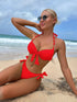 Woman in a red bikini sitting on a beach with ocean waves in the background