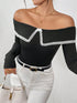 A woman wearing a black off-the-shoulder long-sleeve top with white lace trim, paired with white pants and a black belt, holding a white handbag against a textured white wall.