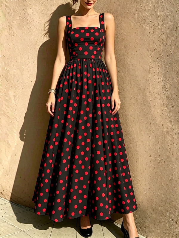 A woman models a sleeveless black maxi dress with a red polka dot pattern, standing against a textured beige stucco wall.