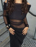 Person wearing a black off-shoulder dress with sheer panels on a concrete surface.