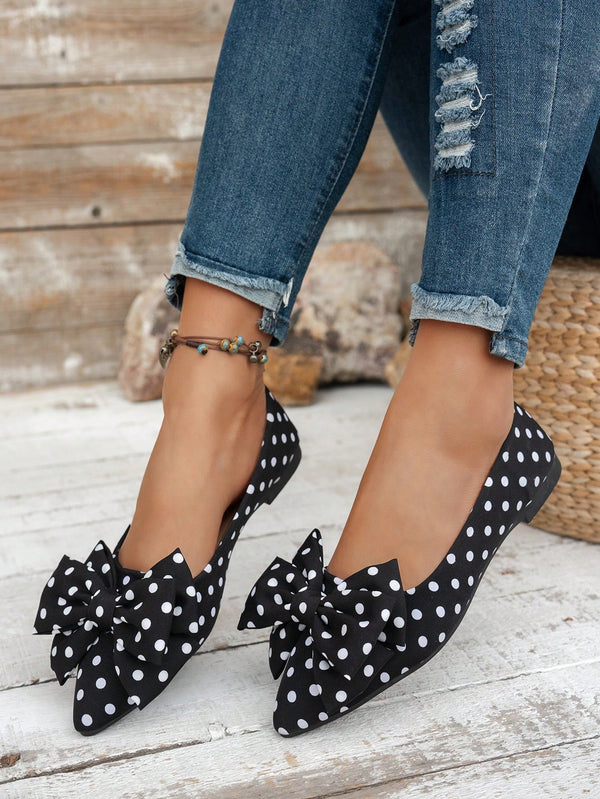 Black polka dot shoes with bows worn with ripped jeans on a wooden floor.