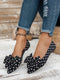 Black polka dot shoes with bows worn with ripped jeans on a wooden floor.