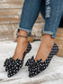 Black polka dot shoes with bows worn with ripped jeans on a wooden floor.