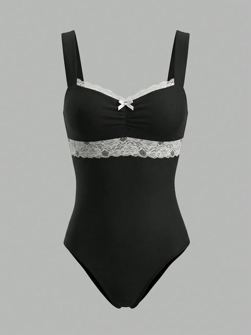 A black one-piece bodysuit with white lace trim across the bust and waist, featuring thin shoulder straps and a small white bow at the center neckline, shown against a solid gray background.