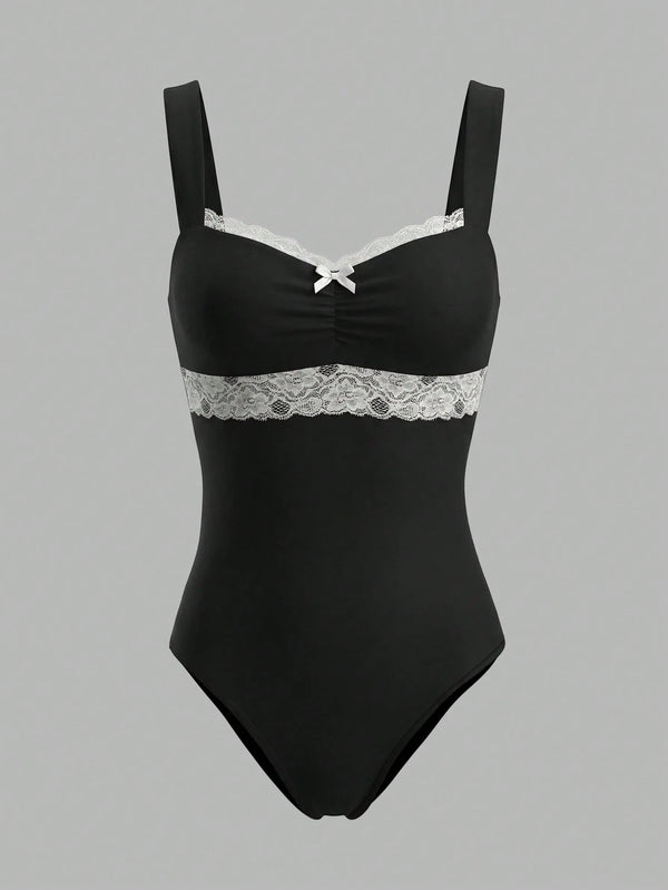 A black one-piece bodysuit with white lace trim across the bust and waist, featuring thin shoulder straps and a small white bow at the center neckline, shown against a solid gray background.