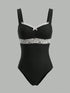 A black one-piece bodysuit with white lace trim across the bust and waist, featuring thin shoulder straps and a small white bow at the center neckline, shown against a solid gray background.