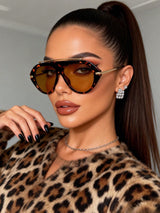 Woman wearing leopard print sunglasses and coat with a neutral background