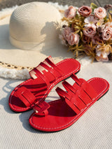 Red sandals on a textured surface with a straw hat and flowers in the background