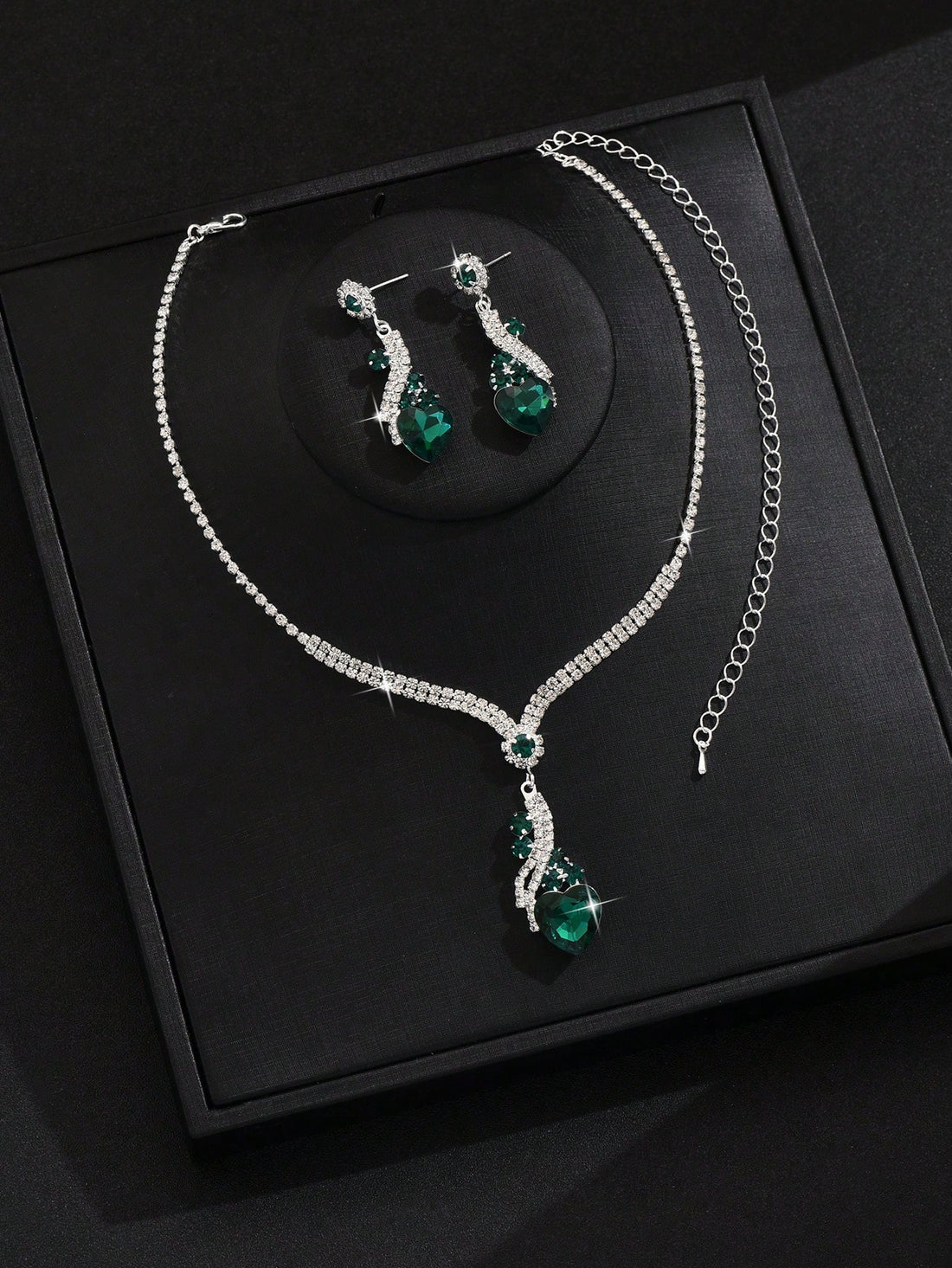 Silver-tone jewelry set featuring a necklace and matching drop earrings with emerald green teardrop stones and clear rhinestone accents, displayed on a black presentation box.