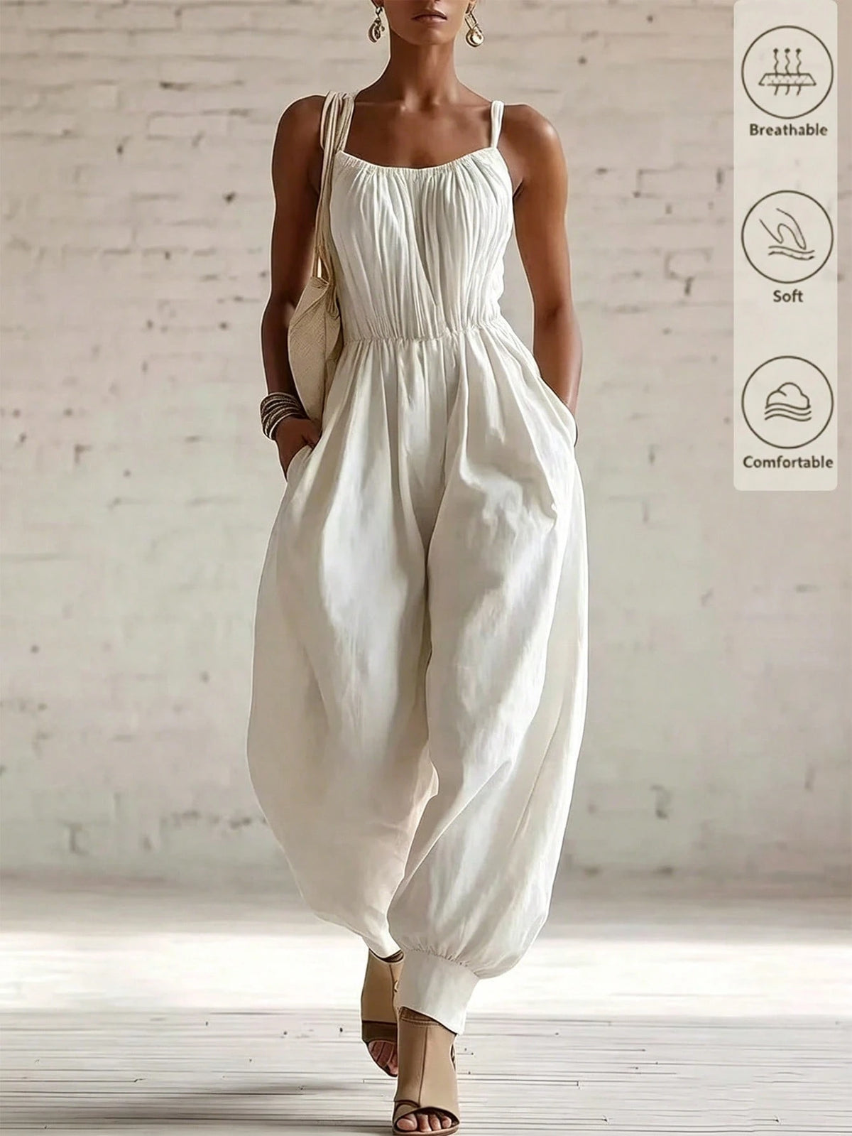 A woman models a cream-colored sleeveless jumpsuit with a gathered bodice and voluminous balloon hems, set against a white brick wall background. A vertical graphic on the right lists product features: breathable, soft, and comfortable.