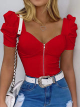 Person wearing a red top with puff sleeves and blue jeans with a white belt.