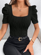 Person wearing a black top with puff sleeves and a belt, sitting on a light-colored couch.